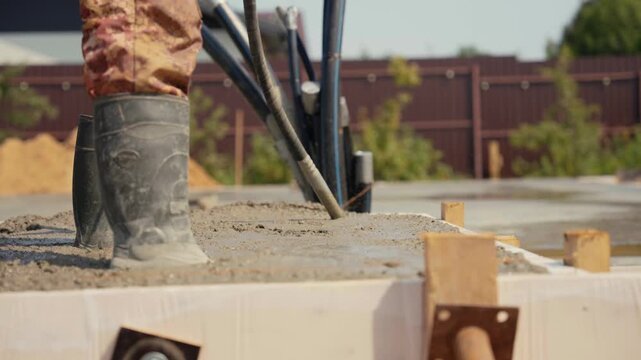 Professional builder using an immersion vibrator to compact freshly poured concrete mix on a building foundation, eliminating air pockets and ensuring a strong, durable structure
