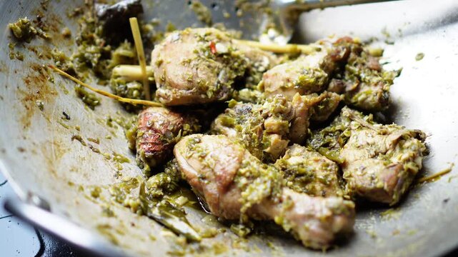 Chicken pieces cooked with vibrant green herb paste in a wok showing rich texture and aroma perfect for culinary content or food preparation scenes, elegantly showcasing cooking.