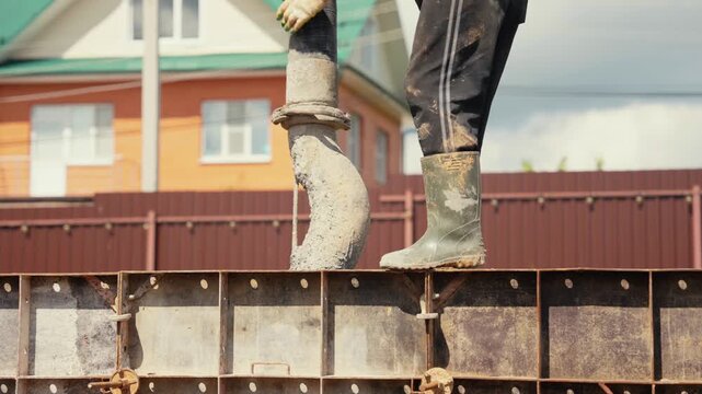 Professional builder pouring wet cement mixture from a concrete pump hose into a metal formwork during the foundation building process at a residential construction site