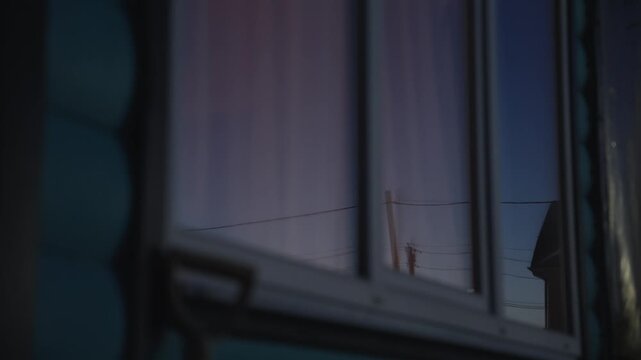 Beautiful evening sky with gradients of pink and blue reflecting in the glass pane of a residential building's window as the light fades, creating a cinematic and moody atmosphere