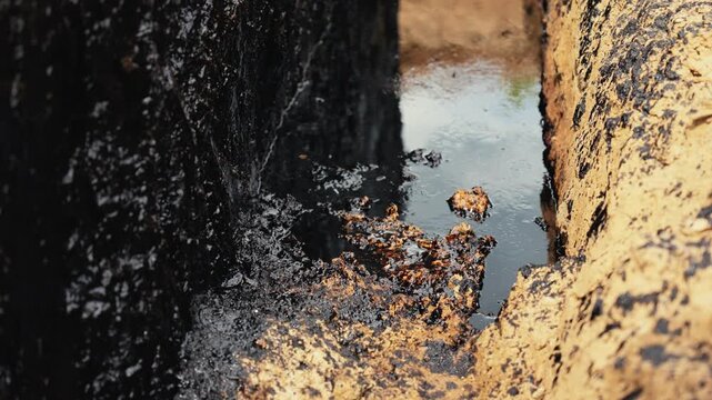 Black viscous crude oil slowly seeping from the earth in a trench, representing environmental pollution, resource extraction, fossil fuels, and industrial contamination of the natural ground