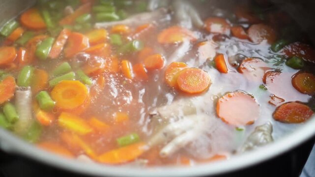 Hearty chicken soup simmering with sliced carrots green beans and chicken feet in a pot rich broth bubbling gently for comforting home cooking meal preparation.