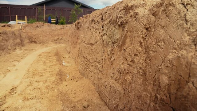 Panoramic view of a deep foundation pit dug in sandy soil for a new residential building, showing the start of the construction process with excavated earth walls ready for development