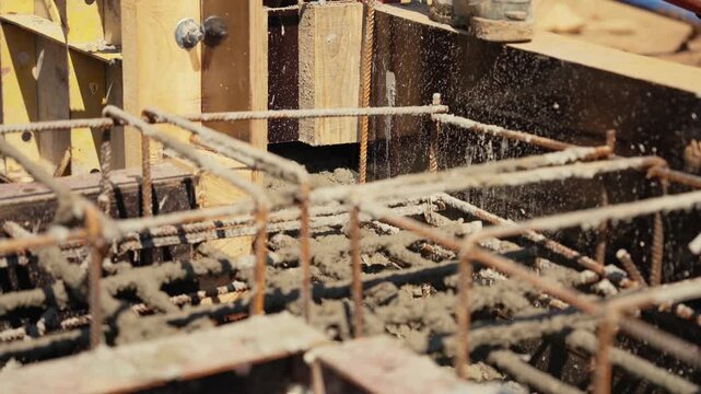 Close up view of workers pouring liquid cement mix into a wooden formwork with a rebar frame, a crucial step in creating a solid building foundation at a construction site