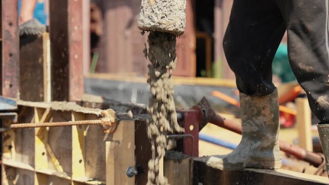 Slow motion footage shows a builder pouring wet cement from a pump hose into a reinforced formwork, a fundamental process in creating a solid building foundation on a construction site