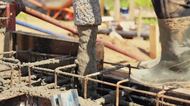 Close up view of a builder pouring liquid cement from a pump hose into a reinforced formwork, creating a solid foundation for a new building during a construction project