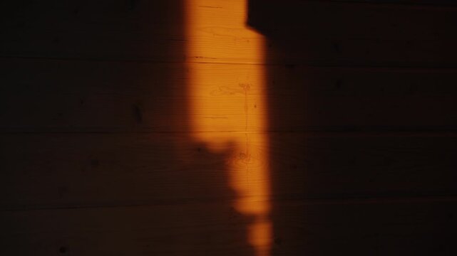 Bright warm ray of sunlight moving across a dark wooden wall, casting a long shadow that changes shape. Orange evening light from a window creating a beautiful, peaceful abstract background