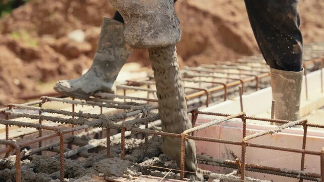 Industrial concrete pump pouring wet cement mix into a reinforced steel cage formwork for a new building foundation, illustrating the initial phase of residential house construction work