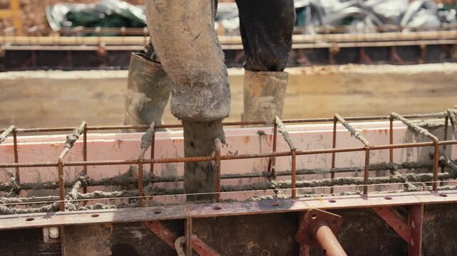 Close up view of a builder using a concrete pump hose to pour wet cement mixture into a reinforced formwork, laying the foundation for a new building at a construction site