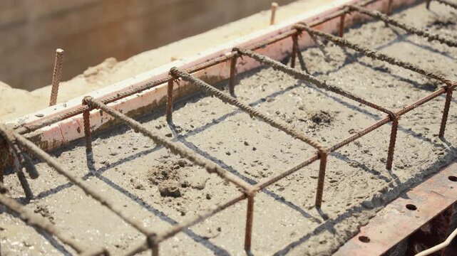 Close up view of fresh wet cement settling and drying within a formwork with reinforcing steel rebar at a construction site, creating a solid and durable building foundation for a new house