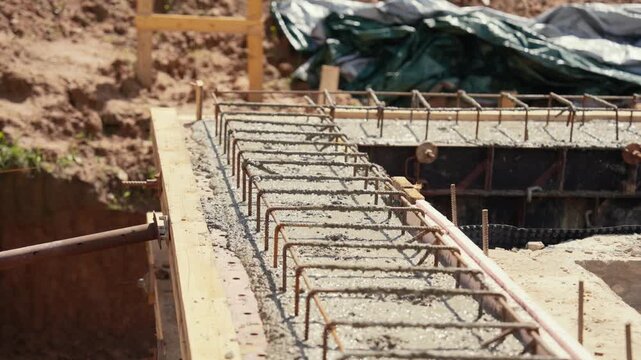 Fresh wet concrete hardening within a wooden formwork and steel rebar frame, forming a sturdy base for a new building during the construction process on a sunny day in slow motion