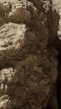 A person explores a cave with large rock formations. The light from outside shines into the cave, revealing textures and shadows. The atmosphere shows the natural stone features.