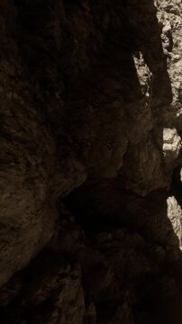 Rocks are stacked in a dark cave. Shadows show the uneven surfaces and textures. The scene looks rugged and natural. Light comes from a small opening above.