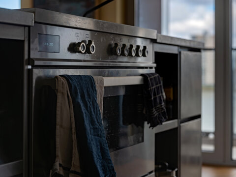 A stainless steel range cooker with knobs and tea towels in a modern kitchen.