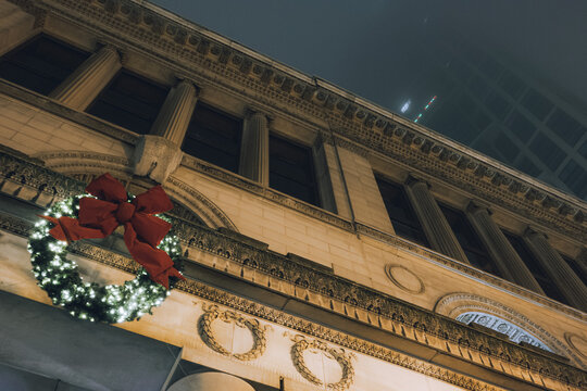 A stunning holiday wreath embellished with bright red ribbons and warm lights, showcasing the festive spirit of the season against a beautiful urban backdrop.