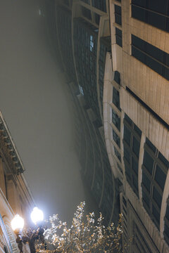 A striking perspective of towering skyscrapers fading into thick fog, highlighting the architectural details and creating a captivating and ethereal scene in the city.