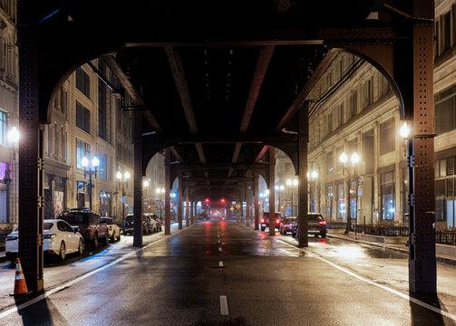A captivating view of a city street beneath elevated train tracks shrouded in mist, showcasing atmospheric lighting and urban architectural details.