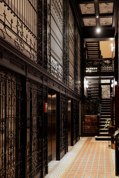 An inviting view of a vintage hallway showcasing decorative elevator lattices and warm lighting, evoking a sense of nostalgia and appreciation for historical architecture.