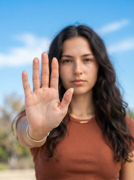 Young woman showing stop gesture with hand. Female model signaling halt or rejection outdoors in casual wear.