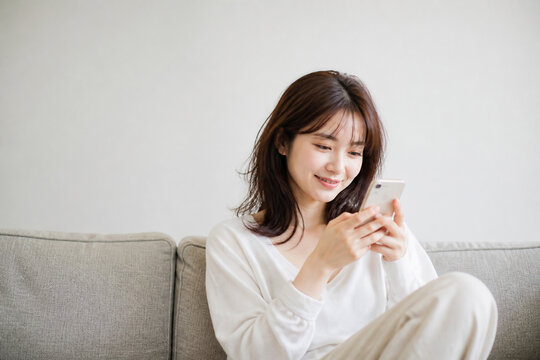 ソファでスマホを見て微笑む日本人女性 Generative AI