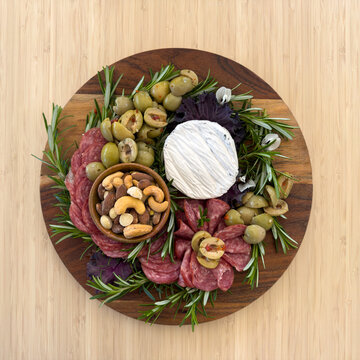 Overhead view of a timber gourmet charcuterie board or cheese platter with various meats, olives, nuts and cheese 