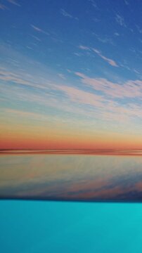 A colorful horizon unfolds as the sun sets over a wide body of water. The sky displays shades of orange and blue. The water reflects the colors of the sky in a still surface.