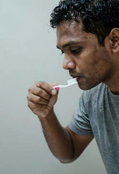 Young adult man brushing teeth with a white and pink toothbrush, oral hygiene and daily routine