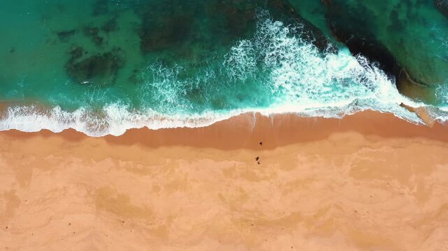 Top down drone view of turquoise Atlantic waves washing onto an empty sandy beach in Portugal.
