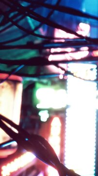 Bright neon lights illuminate a city street at night. Wires hang and create patterns against the colorful signs in the background. The vibrant colors reflect urban life.