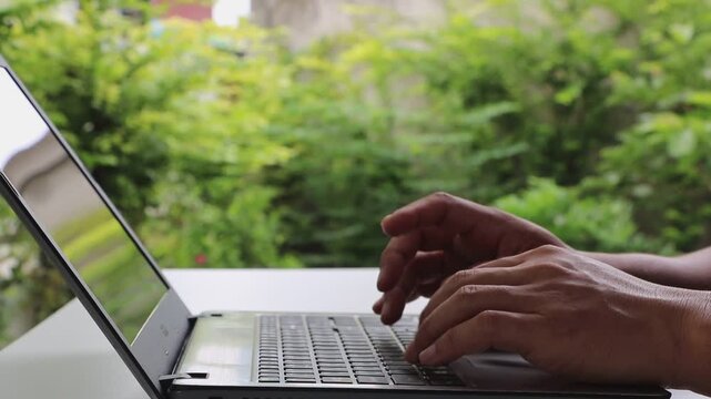 Closeup man's hand is typing on a laptop computer keyboard at home or in the office. He is working, sending messages, chatting, browsing the internet, and using social networking.