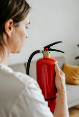 Obraz premium Woman holding a red fire extinguisher, fire safety and emergency preparedness at home or office, close up