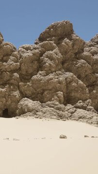 Rocks form large structures in a desert. The dry sand stretches out beneath them. Bright sunlight shines in a clear blue sky. There are no people or objects present in the scene.