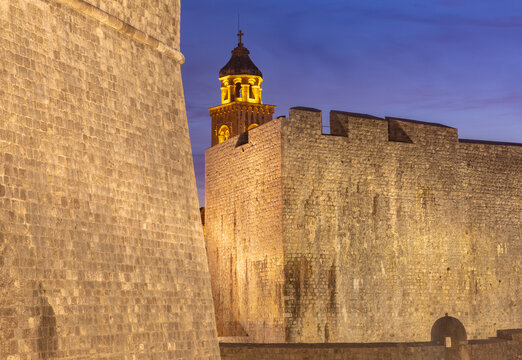 Medieval city walls and illuminated bell tower at blue hour in Dubrovnik Old Town, Croatia.
