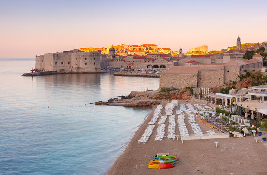 Banje Beach with sun loungers overlooking the historic Old Town and coastal fortifications in Dubrovnik, Croatia, during sunrise.