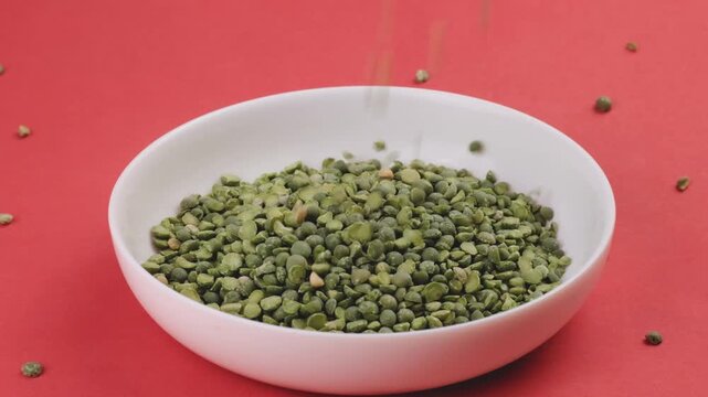 Dried Green Split Peas Pouring into White Ceramic Bowl on Red Background