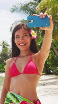 Woman taking smart phone selfie video or photo- Bikini travel girl on beach smiling happy on Matira Beach, Bora Bora. Joyful girl on holidays beach vacation wearing bikini in Tahiti, French Polynesia.
