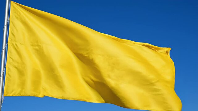 Yellow flag waving on flagpole against clear blue sky, representing warning, caution, or safety status