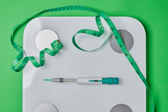 Medical injection pen sitting on a weighing scale with a measuring tape on a green background