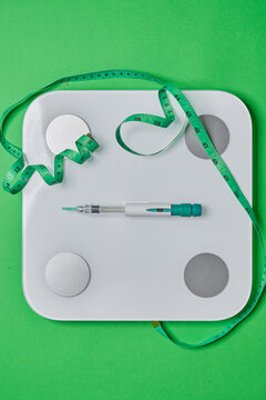 Glp-1 injection pen on a weight scale with a measuring tape, symbolizing weight loss