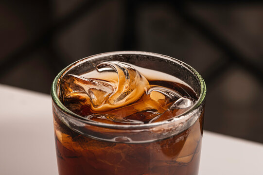 Refreshing glass of dark cola filled with glistening ice cubes, captured in a close-up view. Perfect for representing thirst-quenching drinks, summer beverages, and cafe menus.