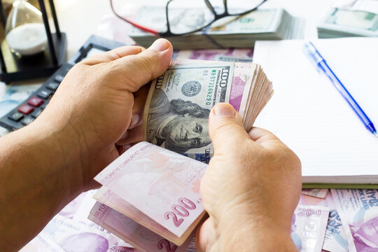 An unknown hand is counting a wad of Turkish money and a hundred US dolar,on the desk.