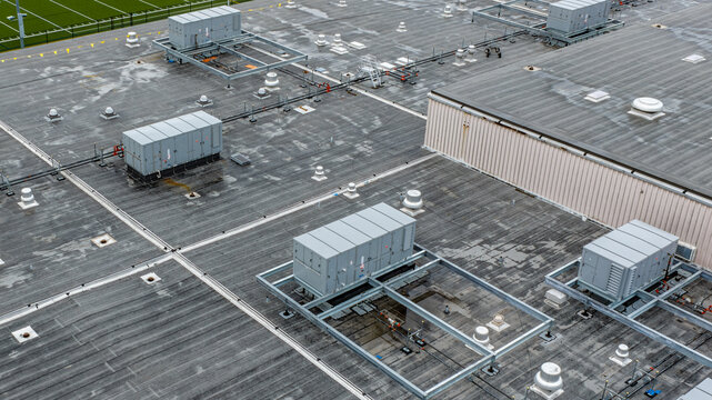 Industrial, commercial HVAC equipment on steel dunnage, and pipes on gray roof.