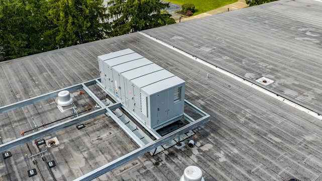 Industrial, commercial HVAC equipment on steel dunnage, and pipes on gray roof.