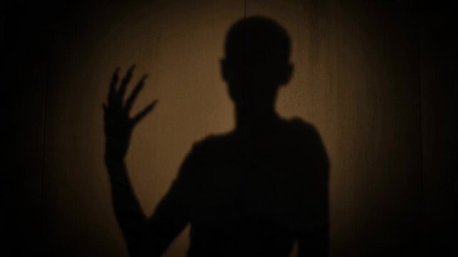 Man shadow cast on wall with unnatural movement. Dark silhouette of male figure displaying eerie gestures. Spooky supernatural motion for mysterious horror theme