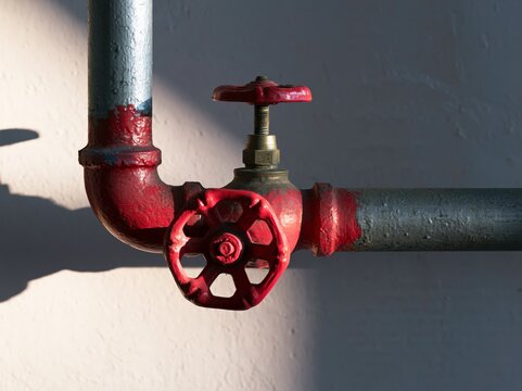 Red fire hose valve on standpipe connection in a building near painted wall