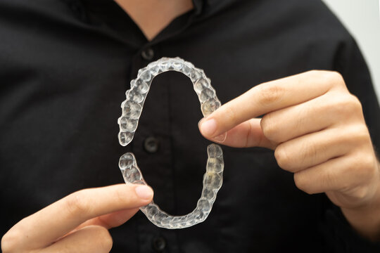 Man holding invisible aligner orthodontic retainer for dental teeth straightening.