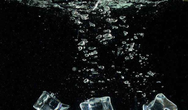 Falling ice cube pieces with water splashing in midair on a transparent, isolated black background. Ice cubes drop into water with air bubbles scatter splashing