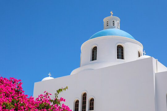 A white church with a blue dome and pink bougainvillea blooms under a clear sky in Santorini, Greece, symbolizing the island&rsquo;s timeless beauty.