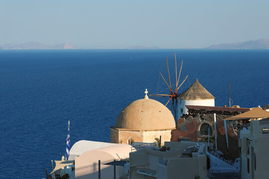 A traditional windmill and domed building overlook the deep blue Aegean Sea in Santorini, Greece, capturing the island&rsquo;s timeless coastal charm.