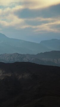 Layers of mountains stretch across the landscape with a cloudy sky above. The scene captures the natural formation and varied terrain. Light plays on the peaks in the distance.
